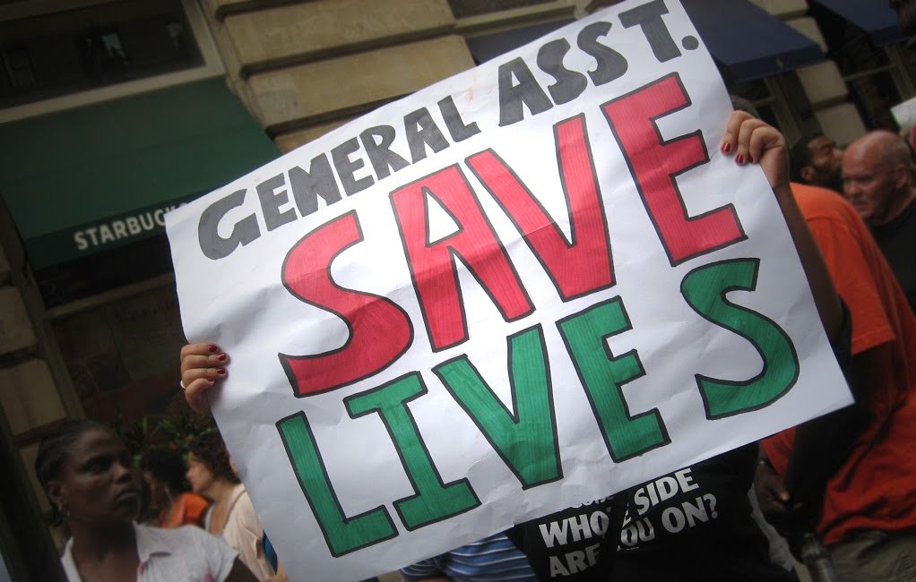 Protester holding sign: Geneal Asst. Save Lives