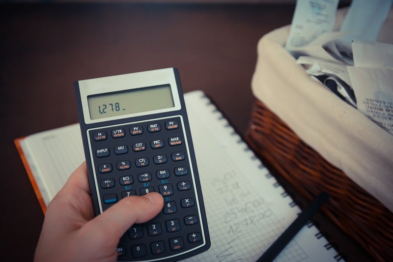 hand holding calculator, stack of bills